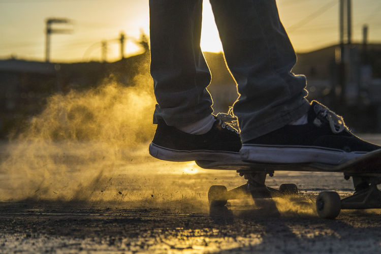 Low section of man skating on road during sunset
