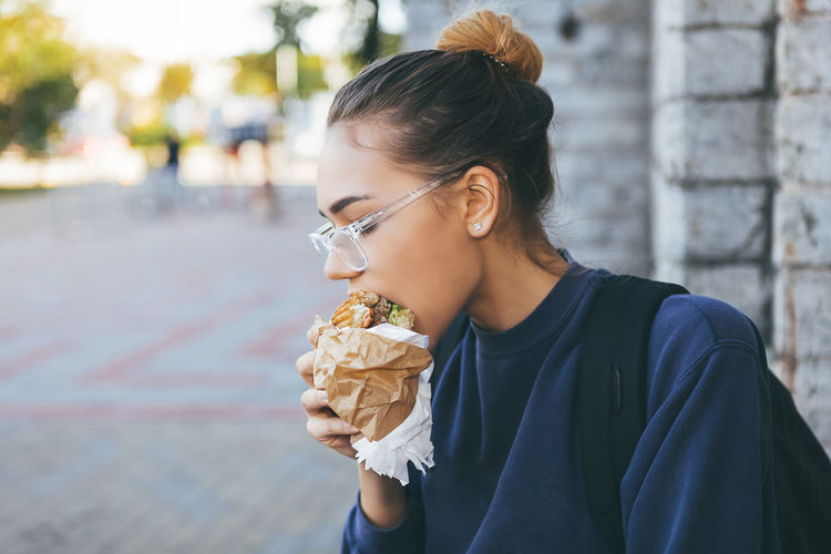 Young woman eating hamburger on street