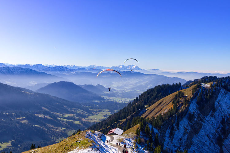 Distant view of people paragliding over mountains against clear sky