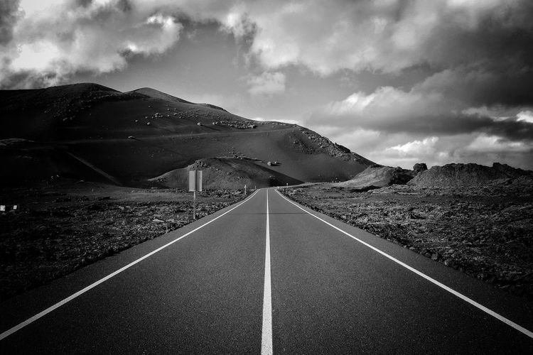 Empty road leading towards mountain range against sky