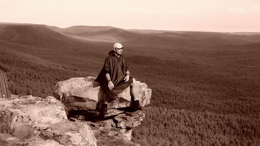 Full length of man sitting on rock against landscape