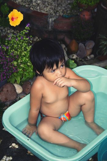 Shirtless boy sitting in bathtub at yard