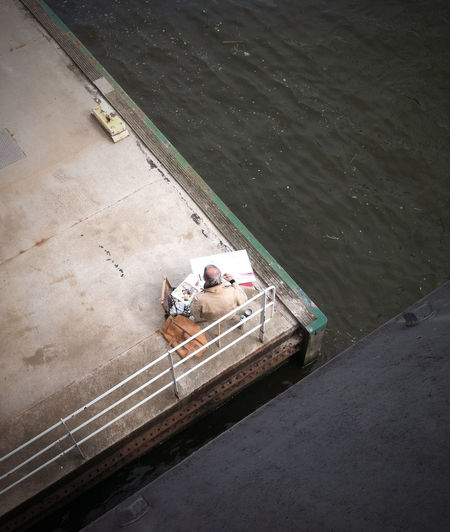 High angle view of painter sitting on pier by sea