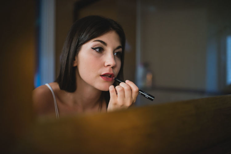 Concentrated charming female with smooth skin applying red lipstick while preparing for event