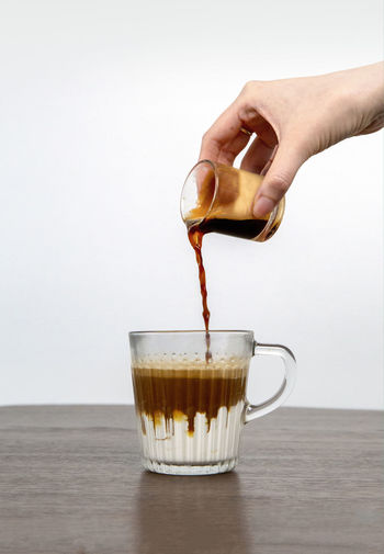 Close-up of hand pouring coffee in glass on table