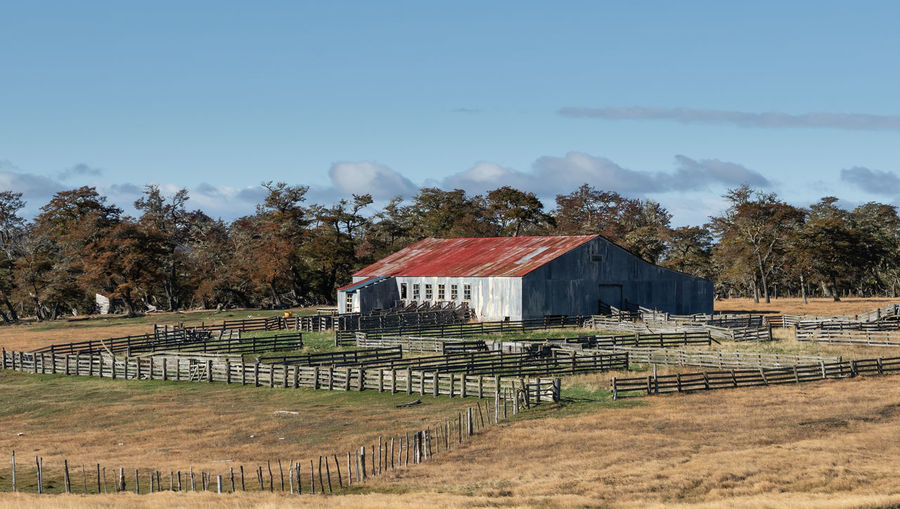 Barn on field by houses against sky