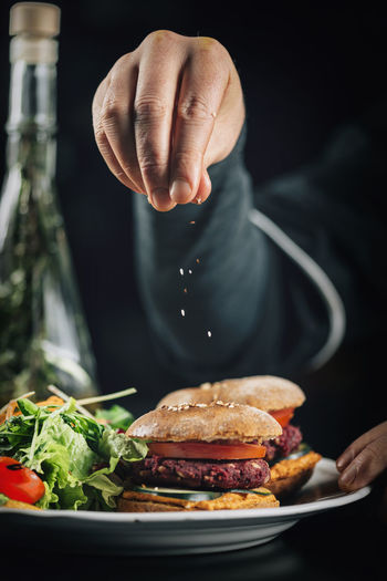 Midsection of chef sprinkling sesame seeds on burger in plate