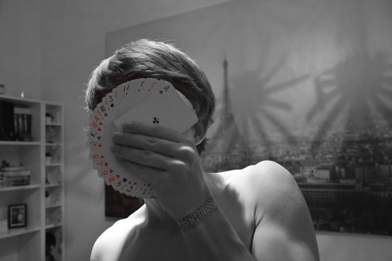 Shirtless man covering face with poker cards