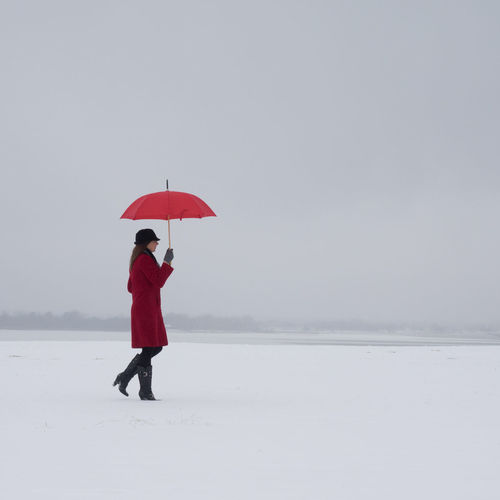 Full length of woman with umbrella standing on snow covered field