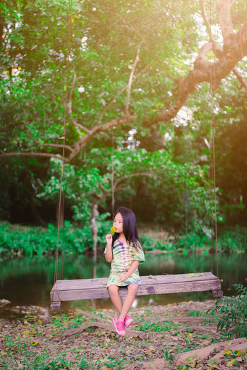 Cute girl holding leaf sitting on swing by lake