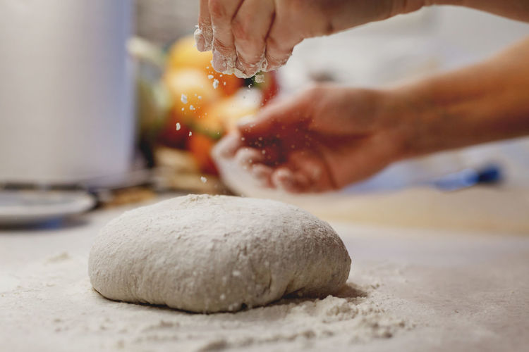 Woman's hands sprinkling flour over freshly kneaded piece of home made bread dough
