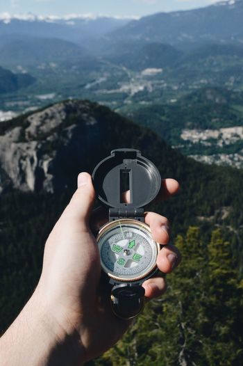 Cropped hand of man holding navigational compass against mountain