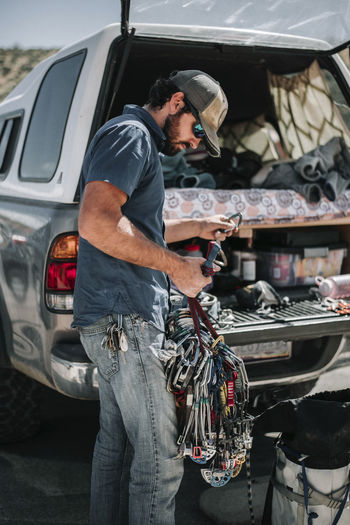 Side view of male hiker holding climbing equipment while standing by off-road vehicle