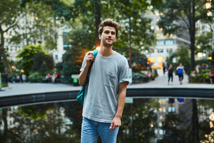 Young man standing by pond in city
