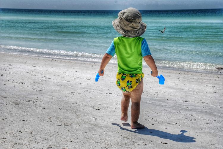 Rear view of toddler walking on sand against sea at beach