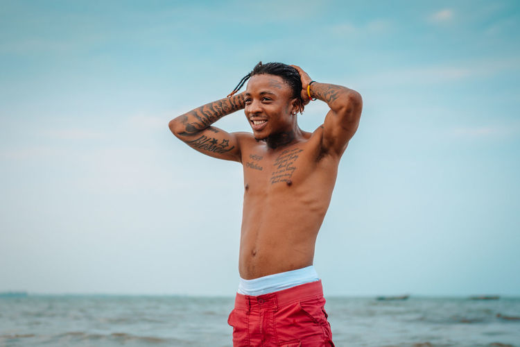 Full length of shirtless man standing at beach against sky