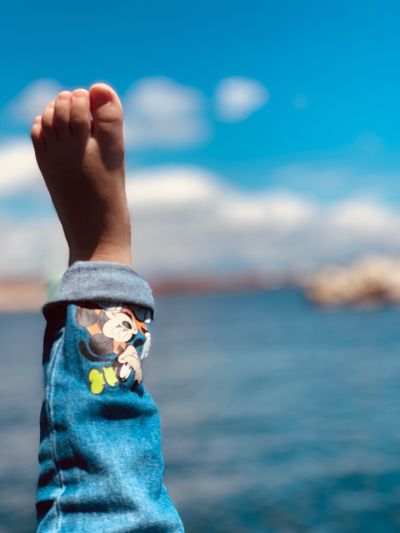 Low section of child against sea and blue sky