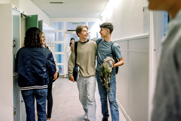 Smiling teenage boys walking together in school corridor