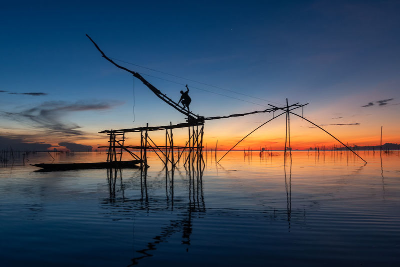 Silhouette fisherman on built structure in sea during sunset