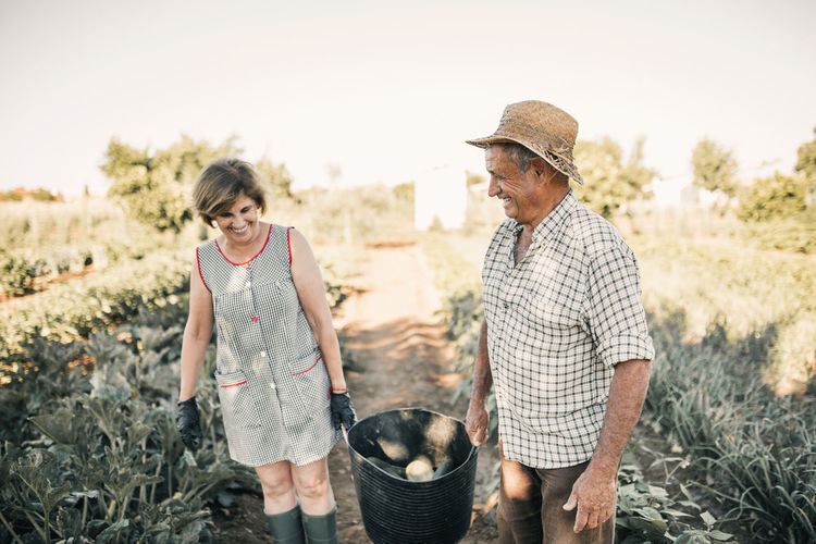 Smiling senior couple holding vegetable basket at farm