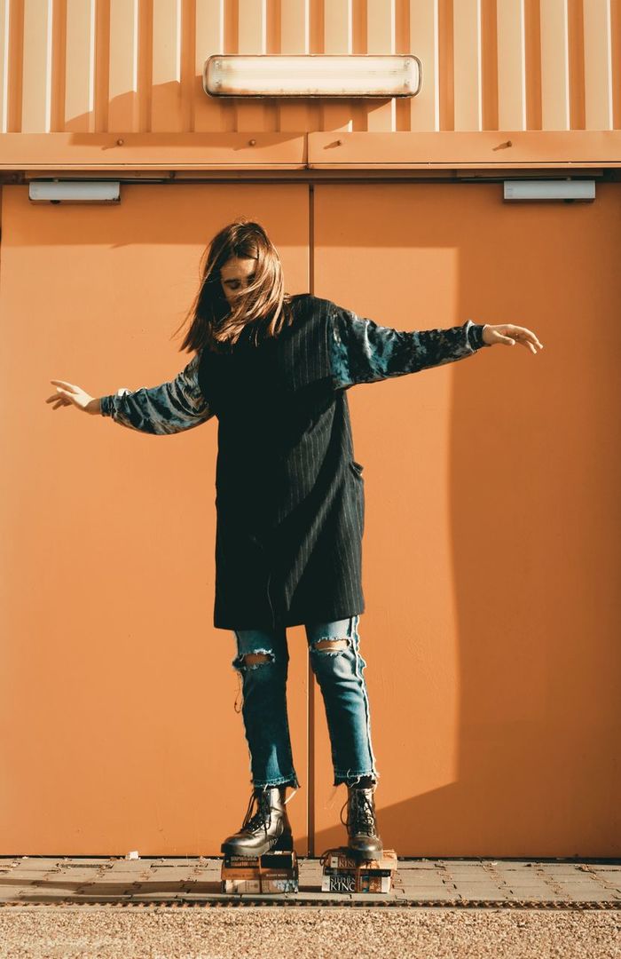 Woman standing on stacked books against orange wall