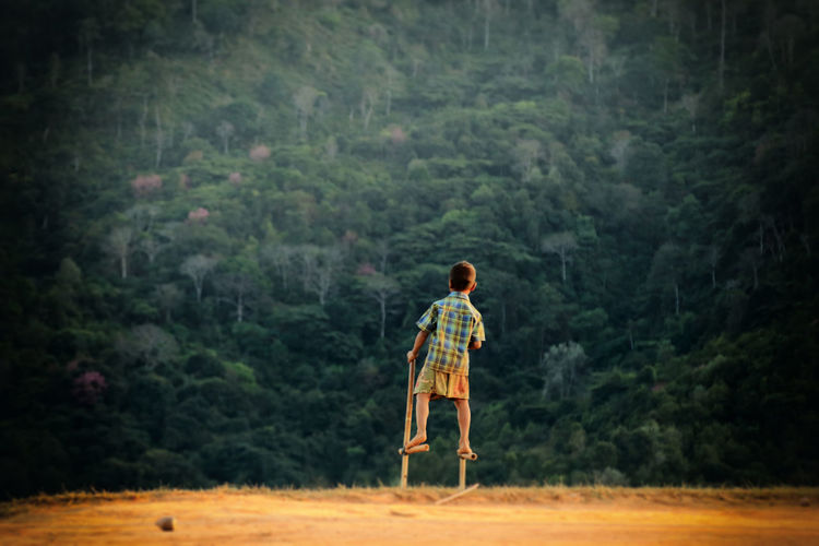 Rear view of boy standing on stilts in field