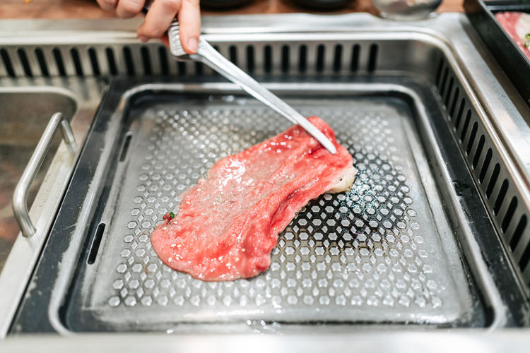Hand grilling a medium rare slice of kagoshima wagyu a5 beef with marble texture with tongs.