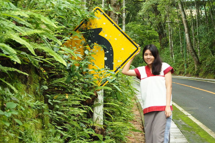 Portrait of beautiful young woman standing by road sign in forest