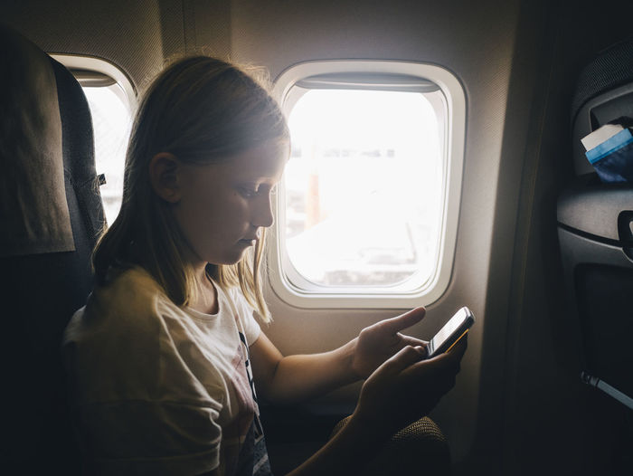 Caucasian girl using mobile phone while sitting by airplane window