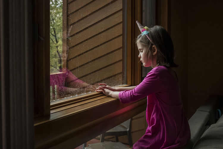 Side view of girl sitting by window at home