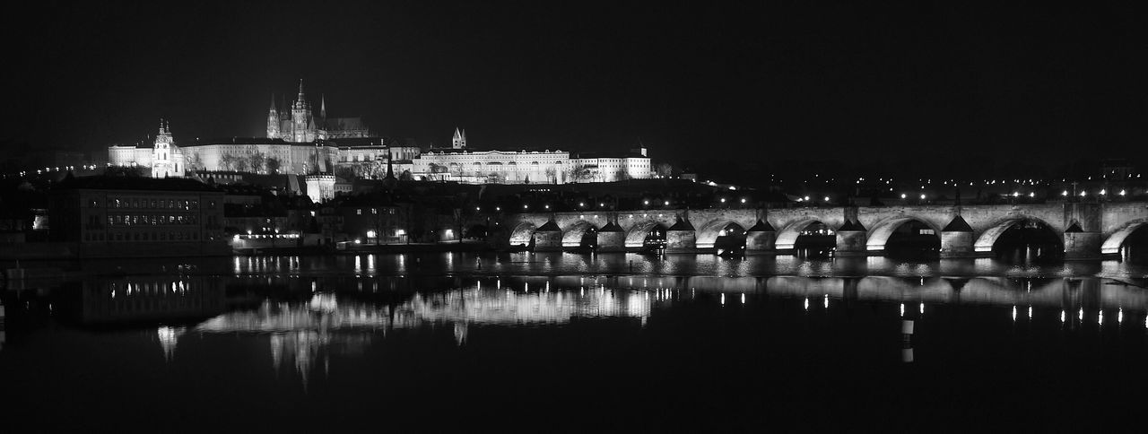 Charles bridge over vltava river against sky in city at night