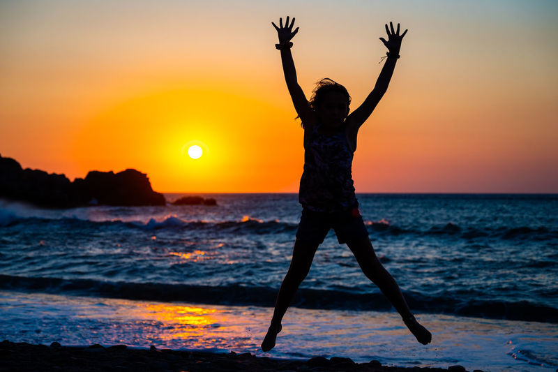 Silhouette woman with arms outstretched standing at beach during sunset