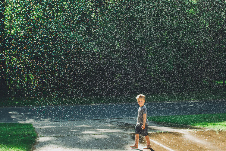 View of boy walking in water drops