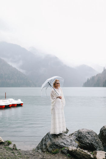 Beautiful young woman bride in a boho dress and with an umbrella stands in the rain in nature