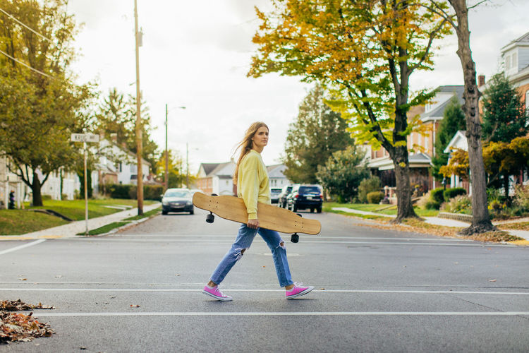 Girl crossing street in small town while holding a longboard with flowing hair