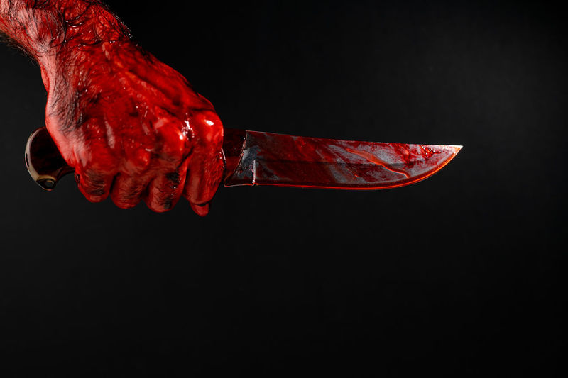 Cropped hand of man holding knife against black background