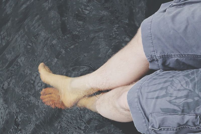 Low section of man dangling feet in water