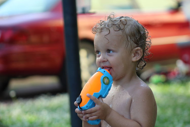 Shirtless boy holding squirt gun while standing outdoors