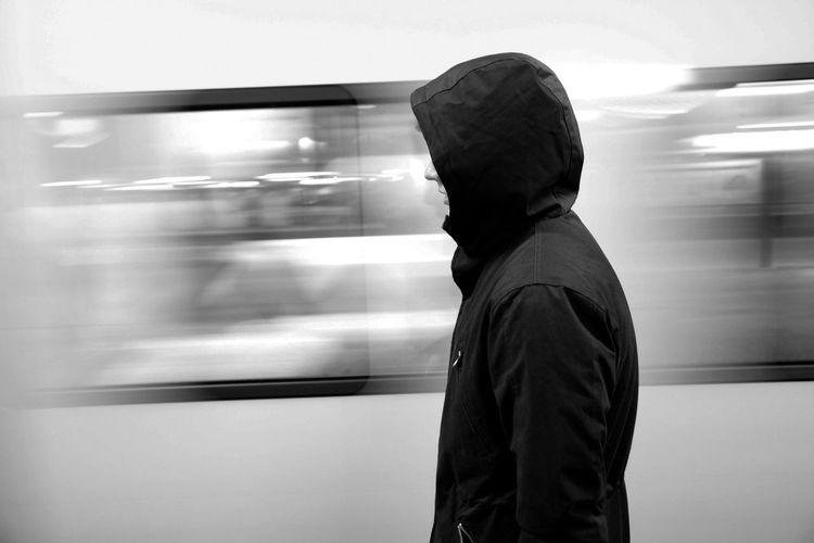 Side view of person in hooded shirt standing by moving train at