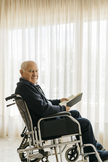 Portrait of smiling senior man sitting in wheelchair with a book