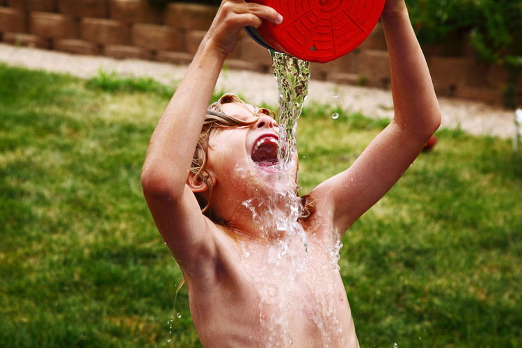 Shirtless boy pouring water on mouth from container at lawn