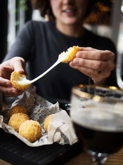 Crop unrecognizable smiling female holding delicious cheese ball with mozzarella filling while sitting at table in cafe