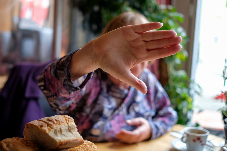 Woman covering her face with hand while sitting by breads on table
