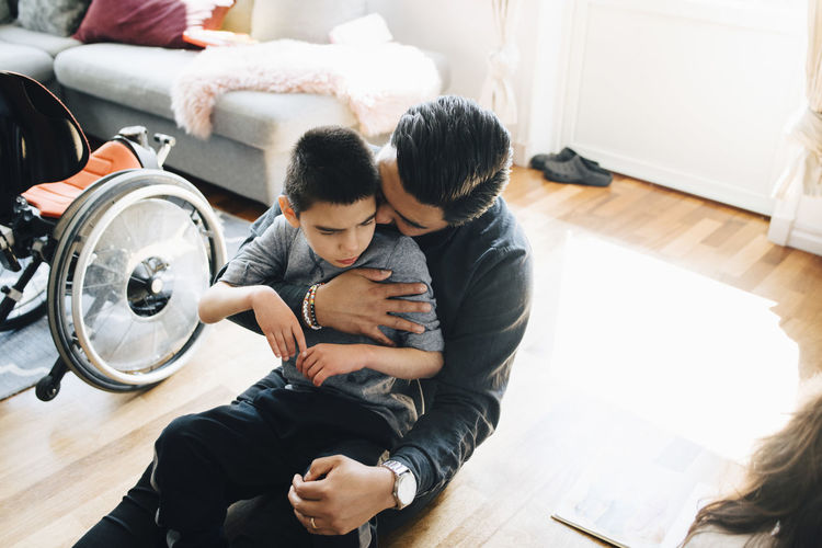 High angle view of father holding autistic son while sitting on floor at home