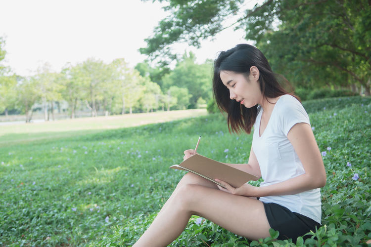 Young woman sitting on book against trees