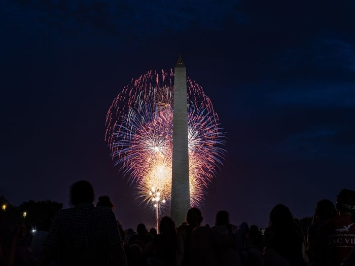 Silhouette people at washington monument against firework display at night