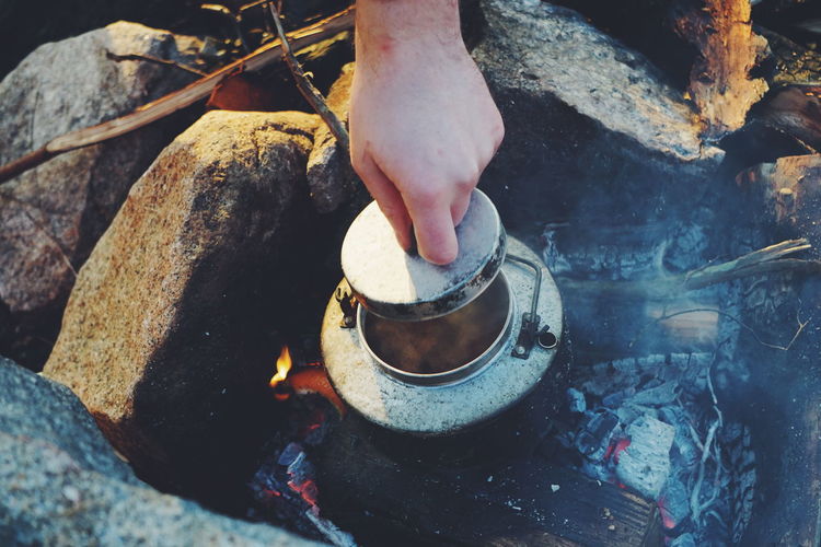 Cropped hand holding lid of container on campfire