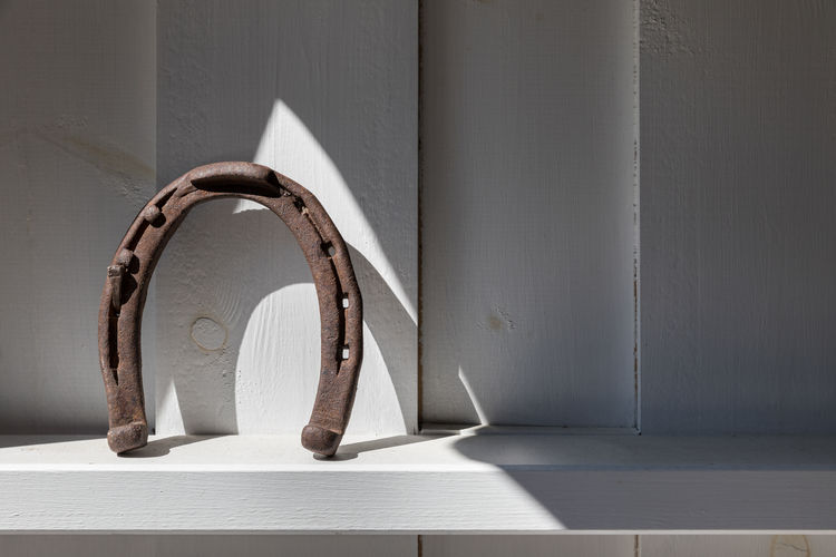 Rusty horseshoe on a white shelf spot lit by sunlight against white wooden wall