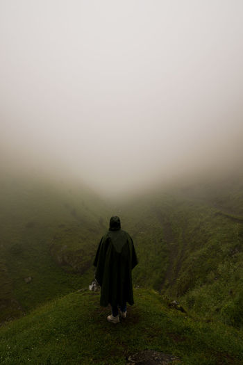 Rear view of man on landscape against sky during foggy weather
