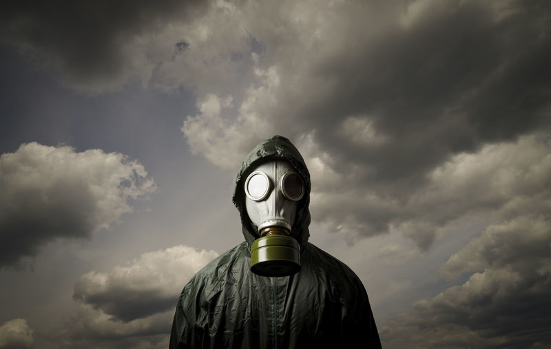 Person wearing gas mask while standing against cloudy sky